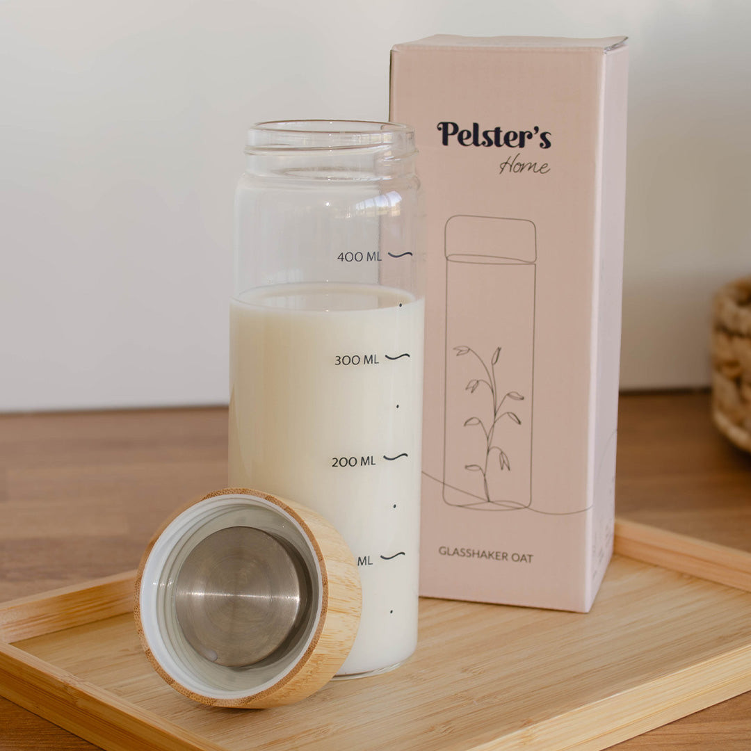 Glasshaker mit hafermilch gefüllt und Verpackung daneben 