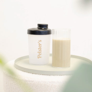 Mini Plastikshaker mit einem von veganem Proteinshake gefülltem Glas